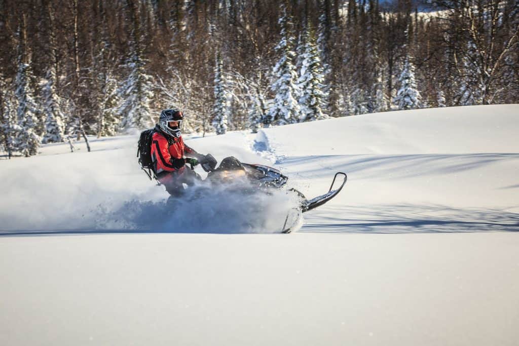 A man fully suited man wearing snow gear while driving his snowmobile