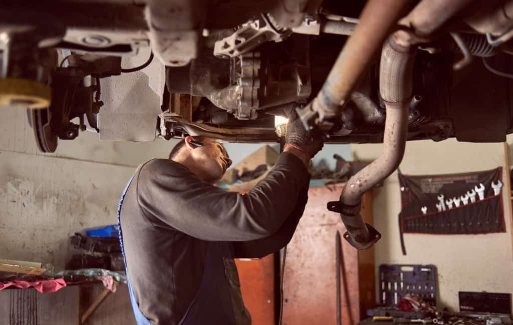 Auto repairman bending under bottom of car while fixing exhaust system of car