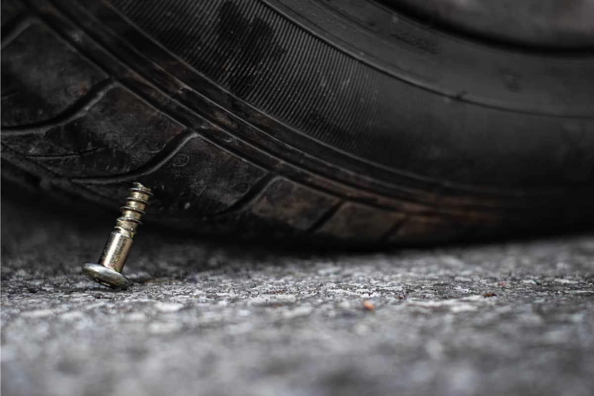 Close up button head needle metal screw nail stuck to puncture into wheel tire on the road