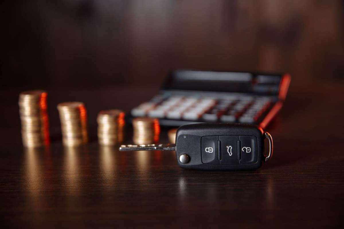 Close-up of car key in front of coins stacked and calculator on wooden table, What Size Battery Does A Nissan Key Fob Take? [And How To Change It]