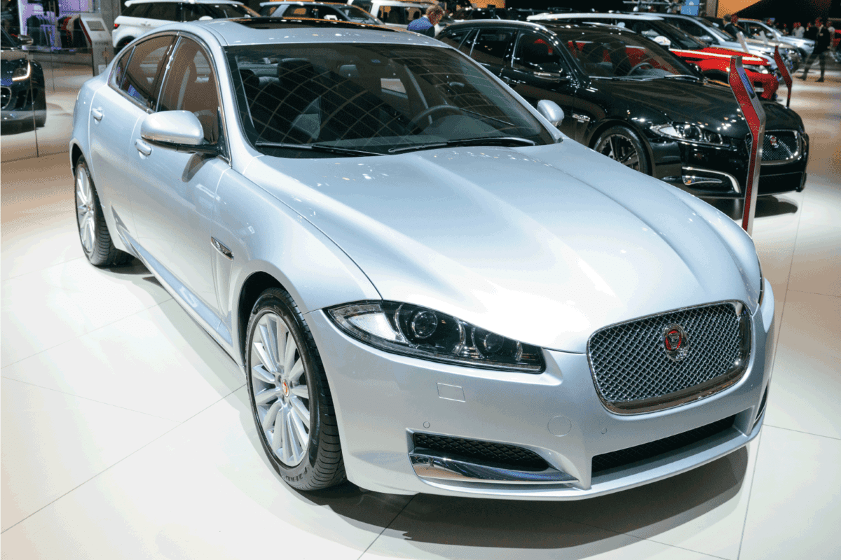 Jaguar XF saloon car on display during a motor show. People in the background are looking at the cars. Does The Jaguar XF Have A Spare Wheel