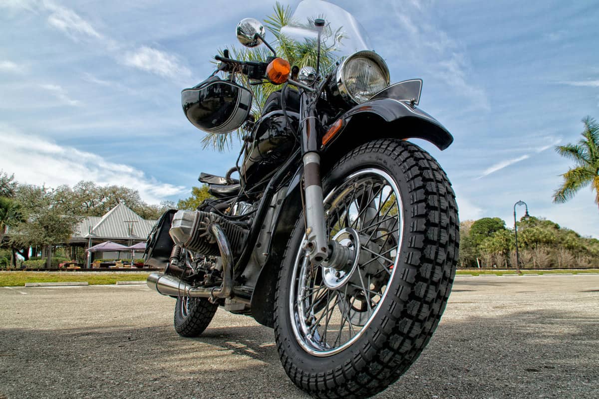 Low angle view black vintage motorcycle the knobby tires and matching helmet hanging from handlebars in tropical florida setting, Should Motorcycle Tires Be Balanced?