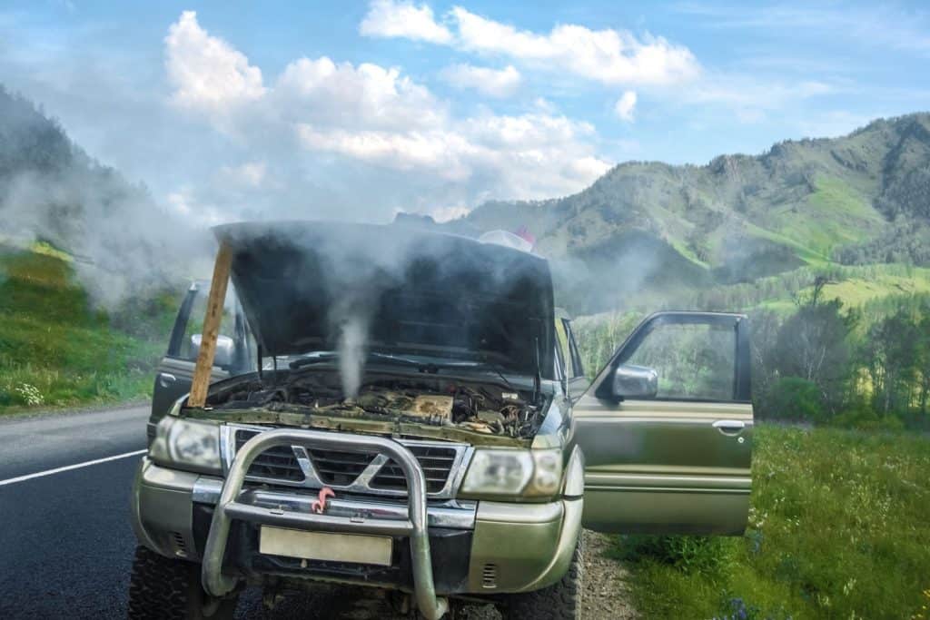 Overheated SUV car standing against summer mountains. smokey car engine
