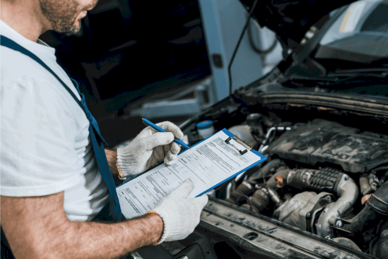 auto mechanic in gloves and cap looking at car engine. Can An Exhaust Leak Cause Misfire