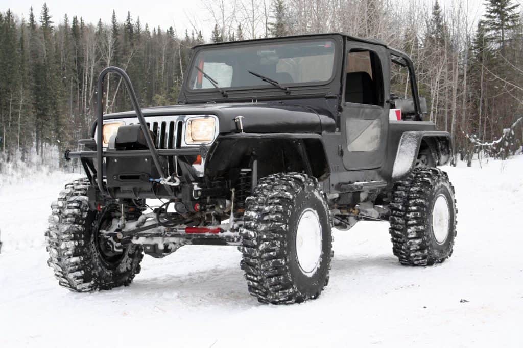 4x4 jeep with agressive tires and winch. Built for off-roading. Parked near and entrance to a 4x4 trail in winter time