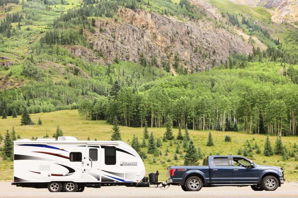 A Ford F-150 towing a travel trailer with a gorgeous mountain landscape on the back