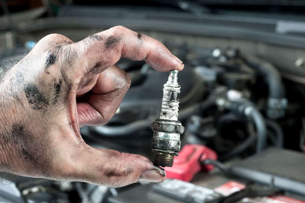 An auto mechanic holds an old, dirty sparkplug over a car engine he is tuning up