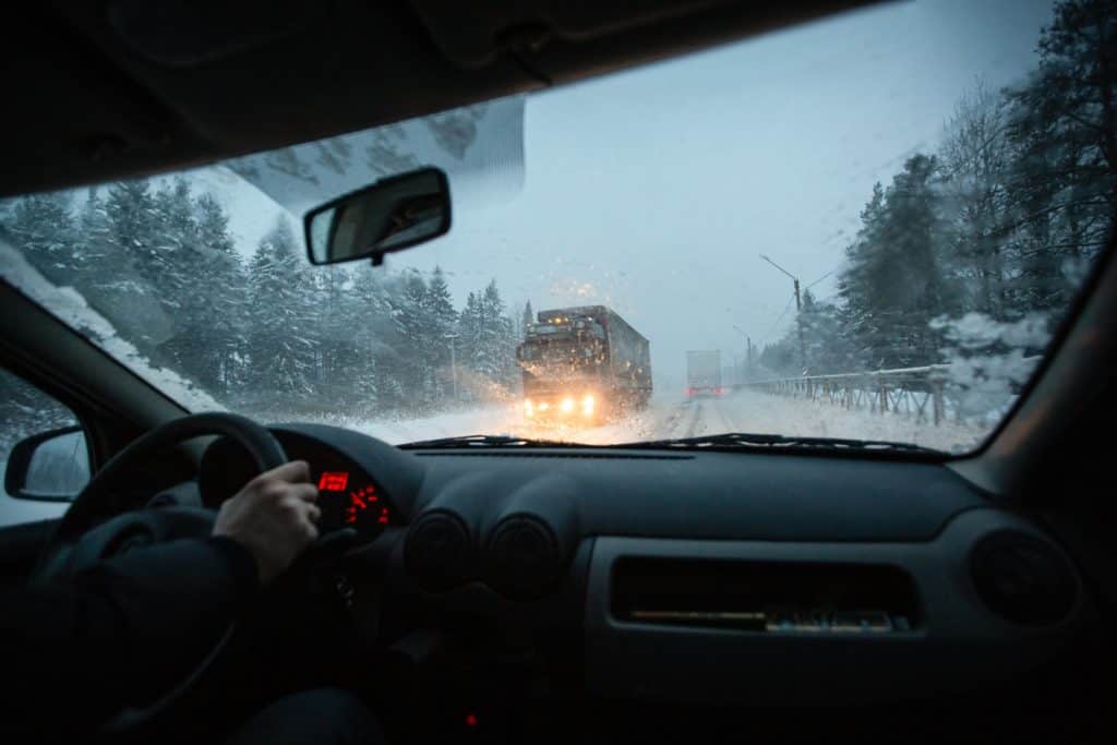 Man drives a car on the winter winter speedway in a snow storm in the twilight when snow with rain is flying. Concept of driving in the dangerous conditions with bad visibility on the winter