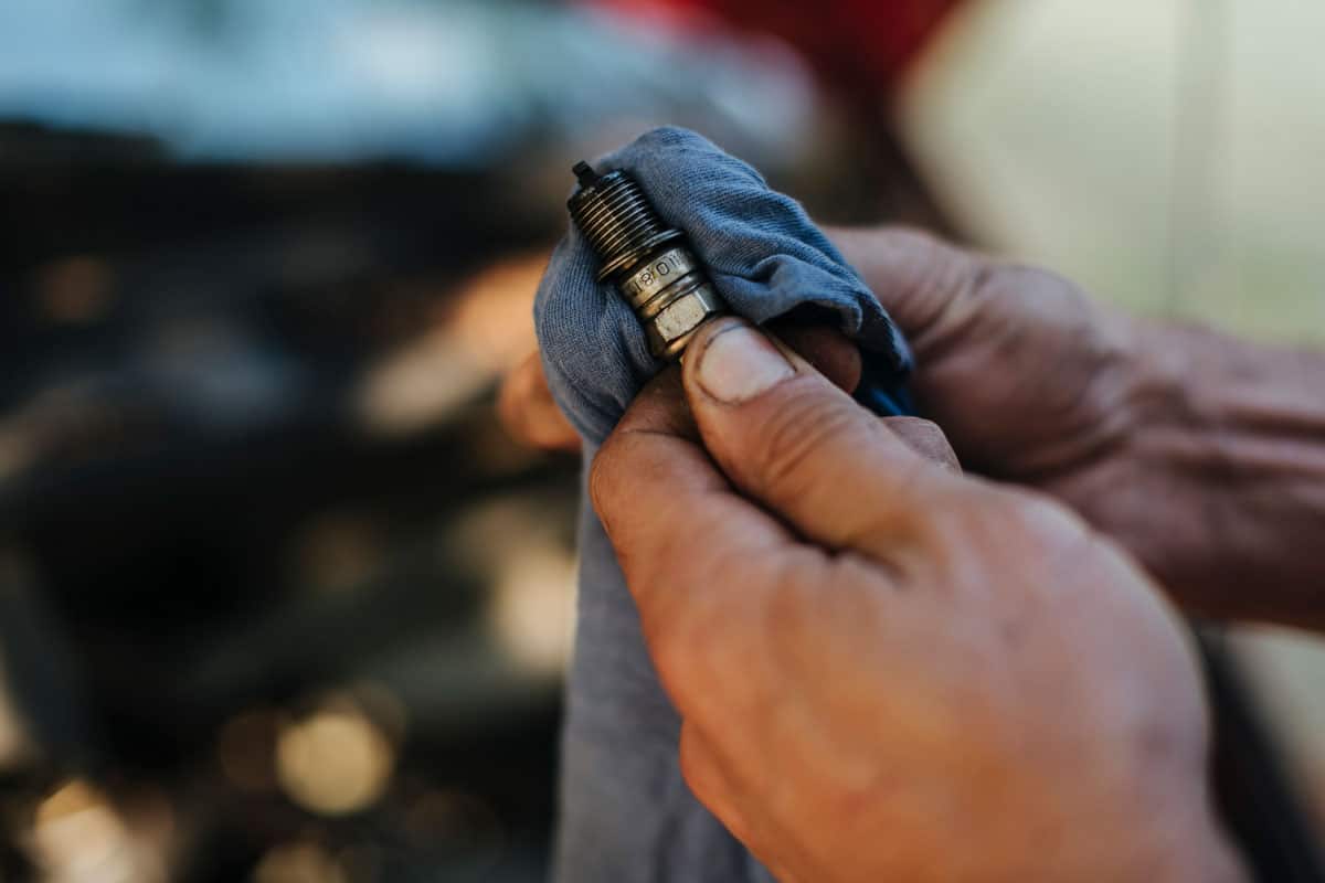 Man checks the spark plug on the old ca while cleaning with cloth