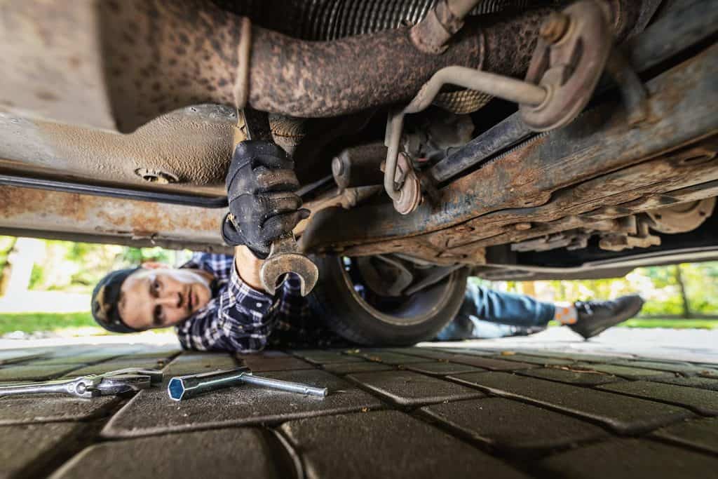 Man laying on the ground under the car and repairing engine with wrench