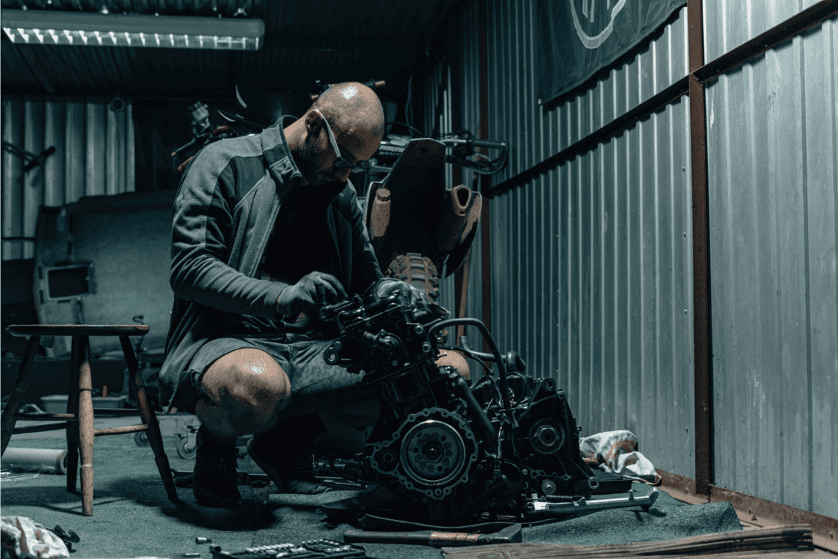Young man repairing his motorcycle engine in the garage. The motorcycle engine is disassembled.