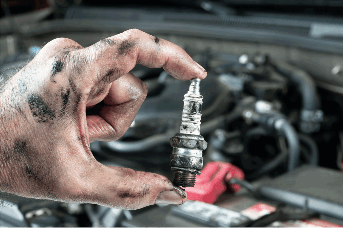 auto mechanic holds an old, dirty sparkplug over a car engine he is tuning up.