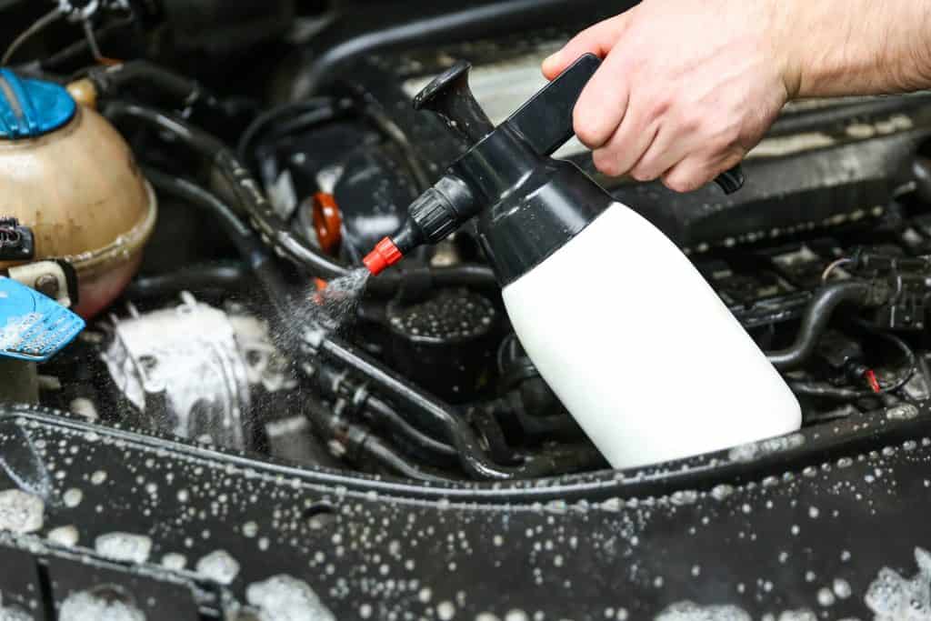 car engine washing close-up. car wash worker apply detergent on car engine. the mechanic's hand holds a spray bottle with detergent over the engine. 