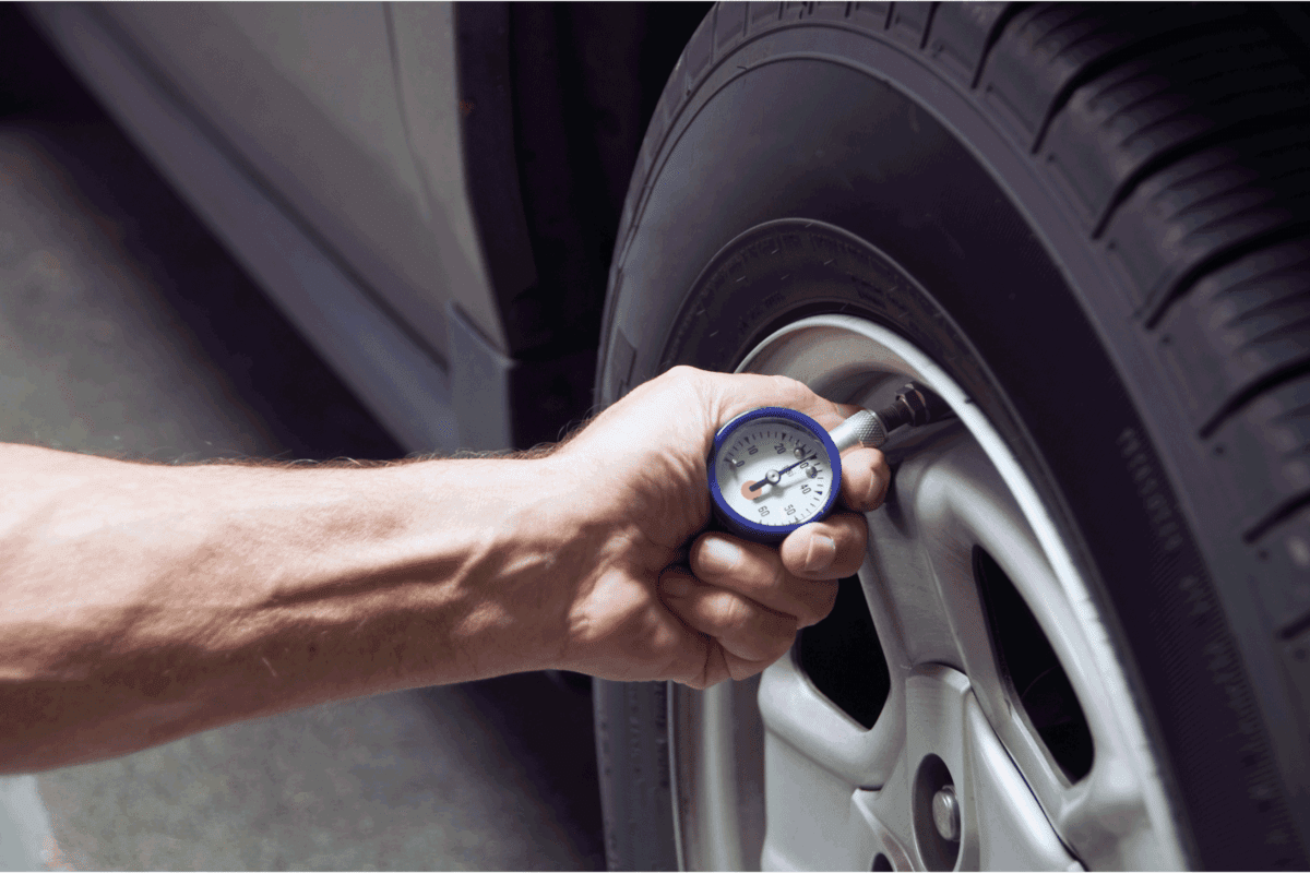 man measuring tire pressure using gauge with dial face