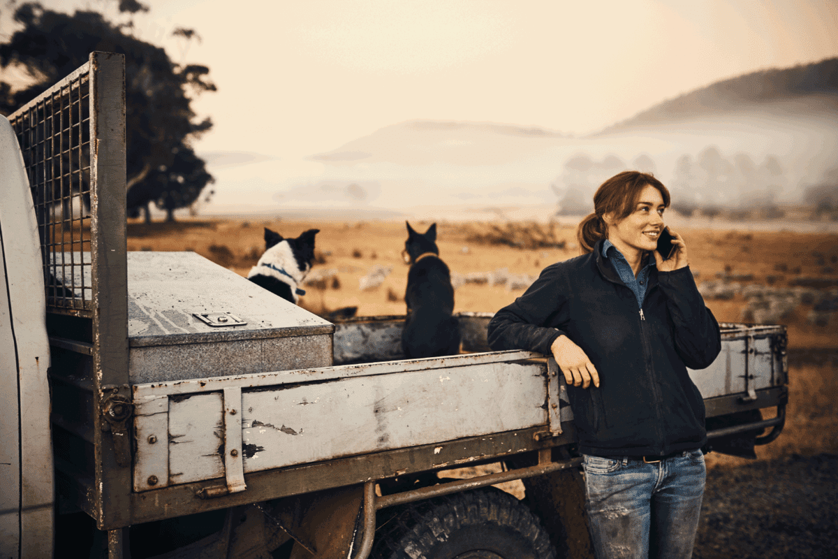 young woman using a mobile phone on her farm beside her flatbed pickup truck