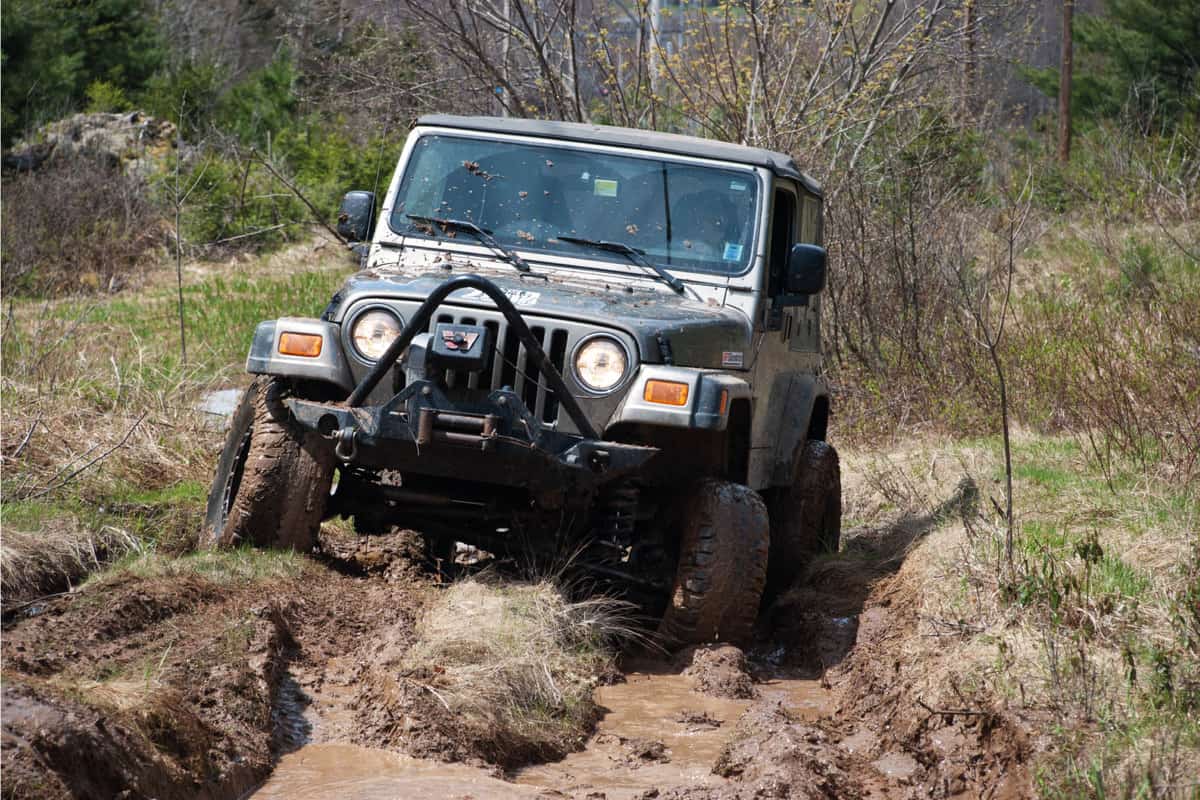 A Jeep Wrangler 4x4 off-roading on a rutted, muddy trail.
