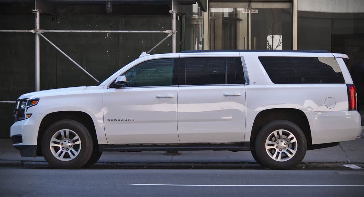 A full-sized white Chevy Suburban parked near a building
