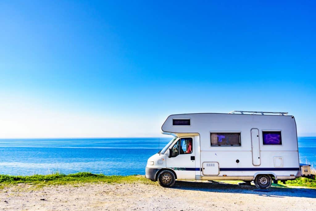 A small RV parked near the cliff for a scenic view of the ocean