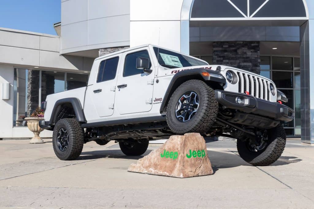 A white Jeep Gladiator with its front wheel raised on an artificially made rock