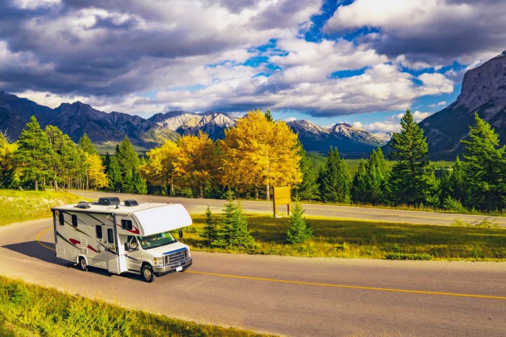 A whtie Class B motorhome traveling on a curved path with a scenic view of a mountain range on the back