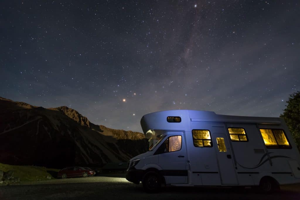 An RV parked under the bright and clear night sky with millions of stars visible