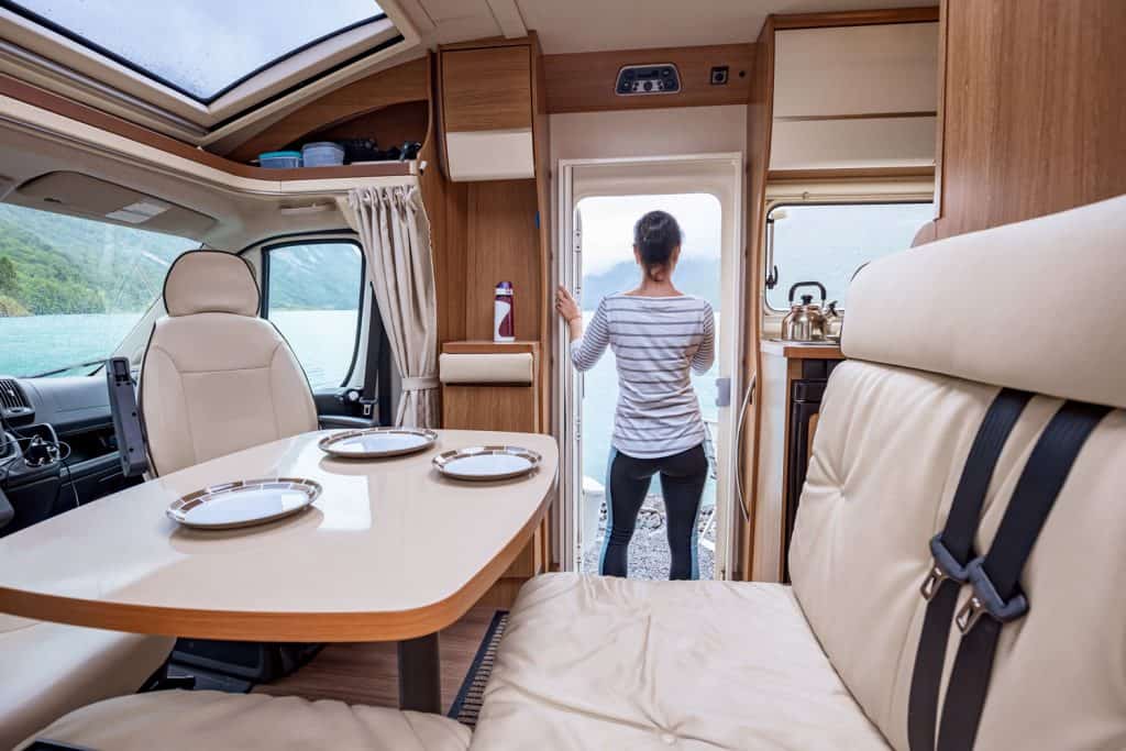Modern themed interior of a Class A motorhome with a small dining area and natural lighting from the windows