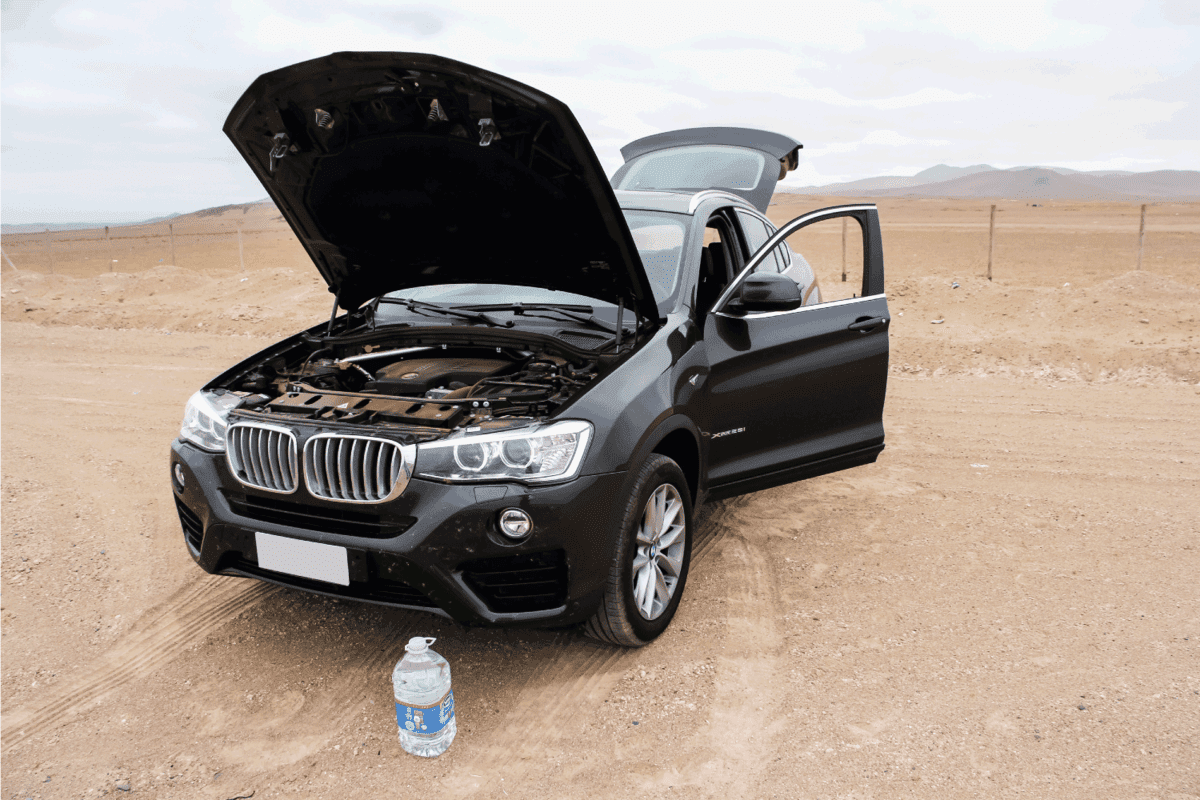 Motor car BMW F26 X4 with an opened bonnet is parked in the desert.