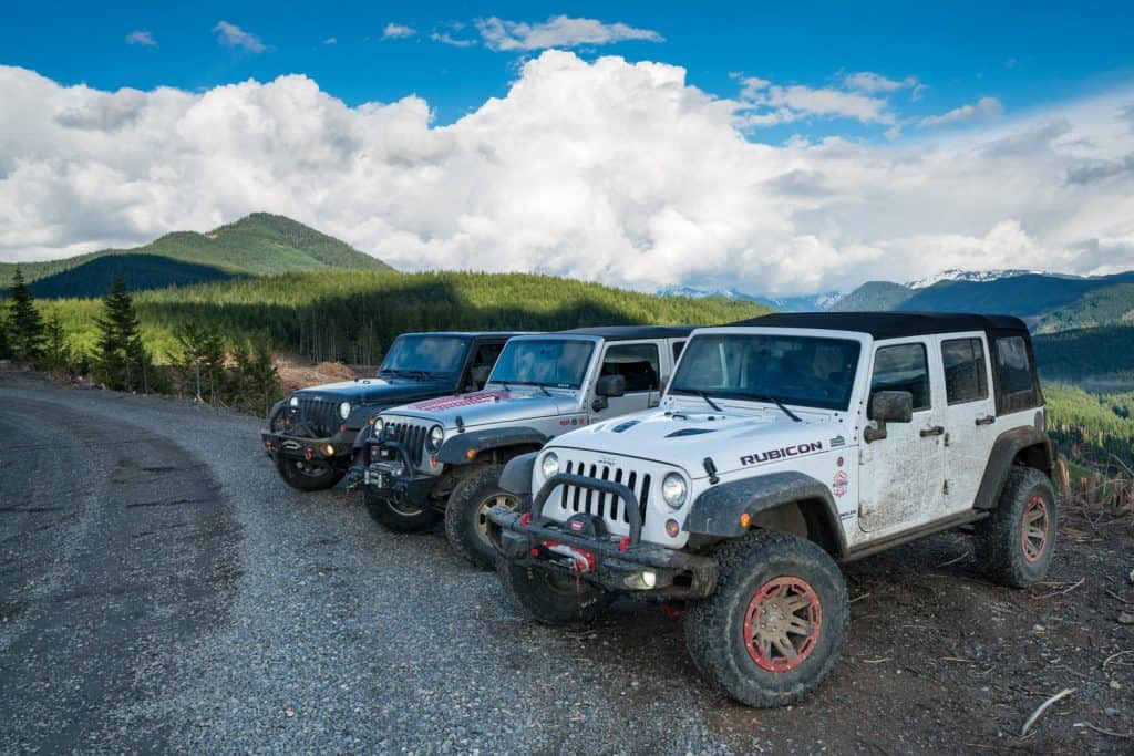 Three Jeep Gladiators parked near a cliff and photographed with a scenic view of the mountain range 