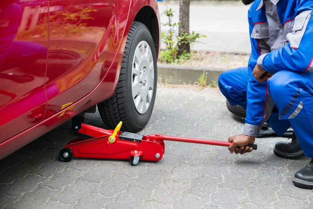 A car mechanic using a floor jack to raise the red car