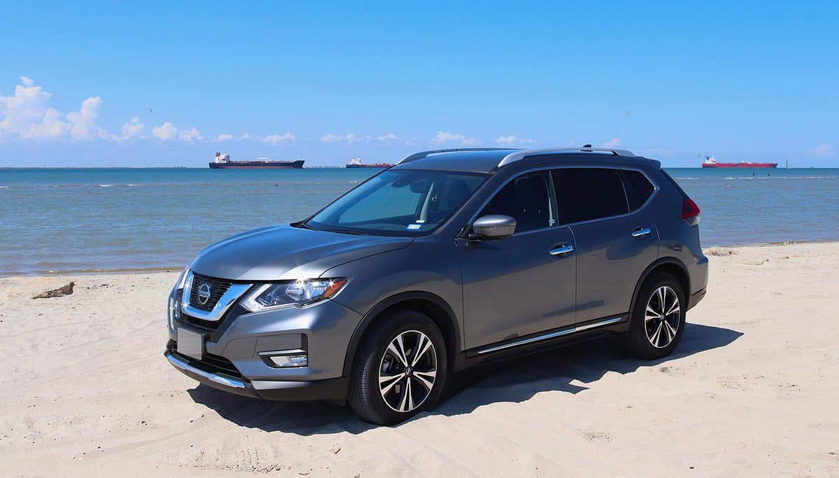 A charcoal gray colored Nissan Rogue compact crossover SUV car is parked on the beach