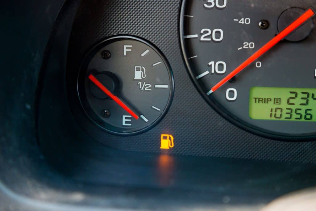A gas guage in a car reads empty and shows the warning light to let the driver know they are out of gas and need to refuel
