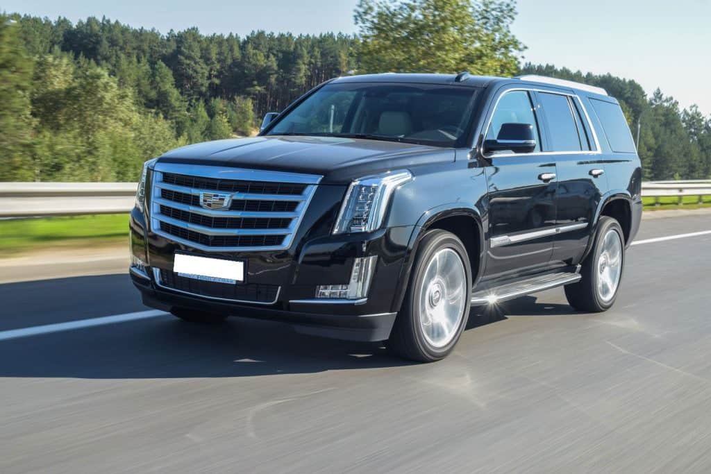  Cadillac Escalade drives on a road during a sunny day.