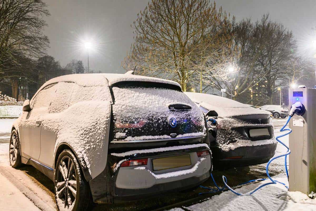 Electric cars charging at an electric vehicle charging station during a cold snowy winter night