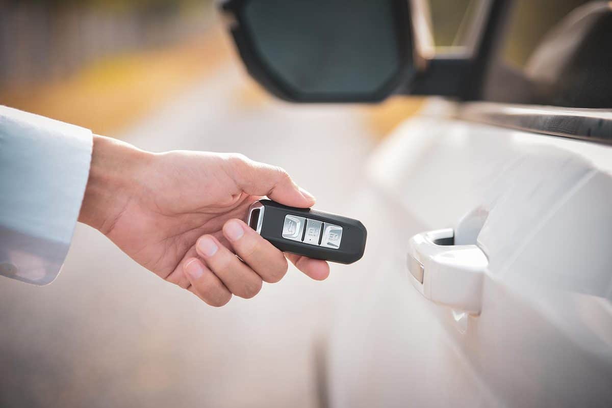 Hand holding smart key to lock doors of white car