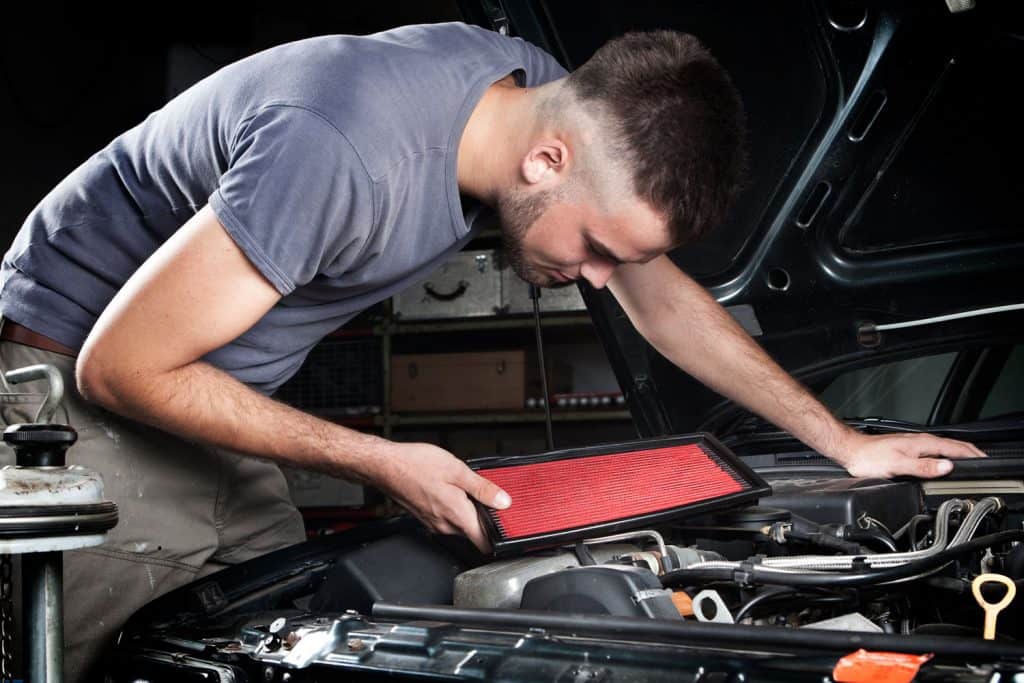 Handsome mechanic is repairing the engine bay of an old car - checking the air filter
