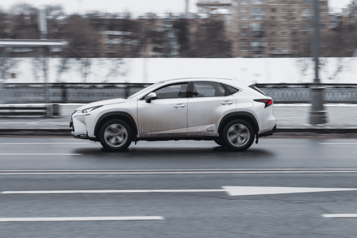  Side view rolling shot with white crossover car in motion. Lexus NX 200T driving along winter street in city