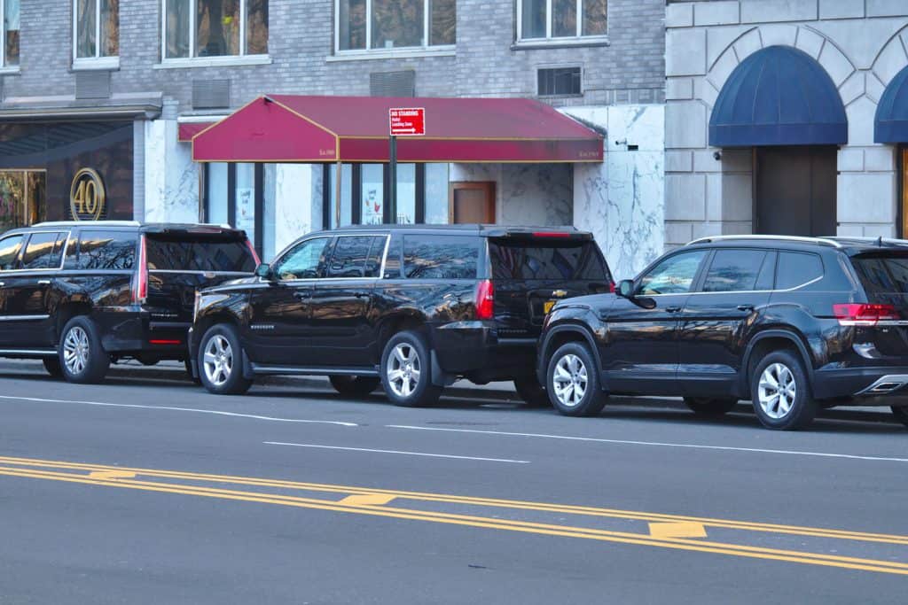 Three huge black SUVs parked outside a hotel