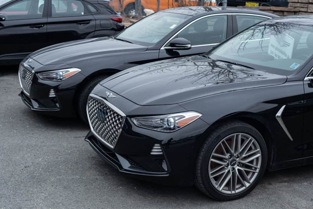 Two black Genesis G70 photographed at a parking lot