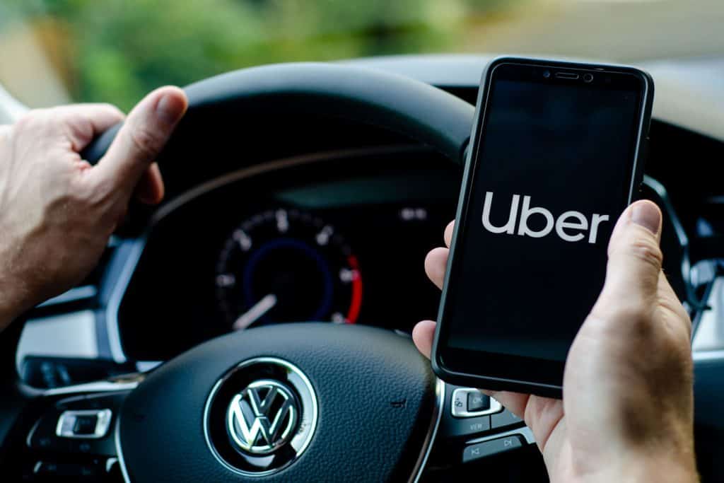 Uber driver holding smartphone in Volkswagen car, Can You Uber With Someone Else's Car?