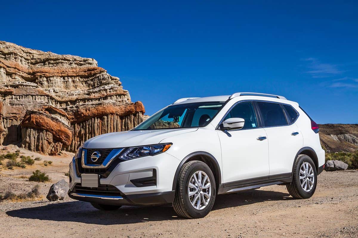 White Nissan Rogue on gravel road in front of sandstone formation in desert wilderness area