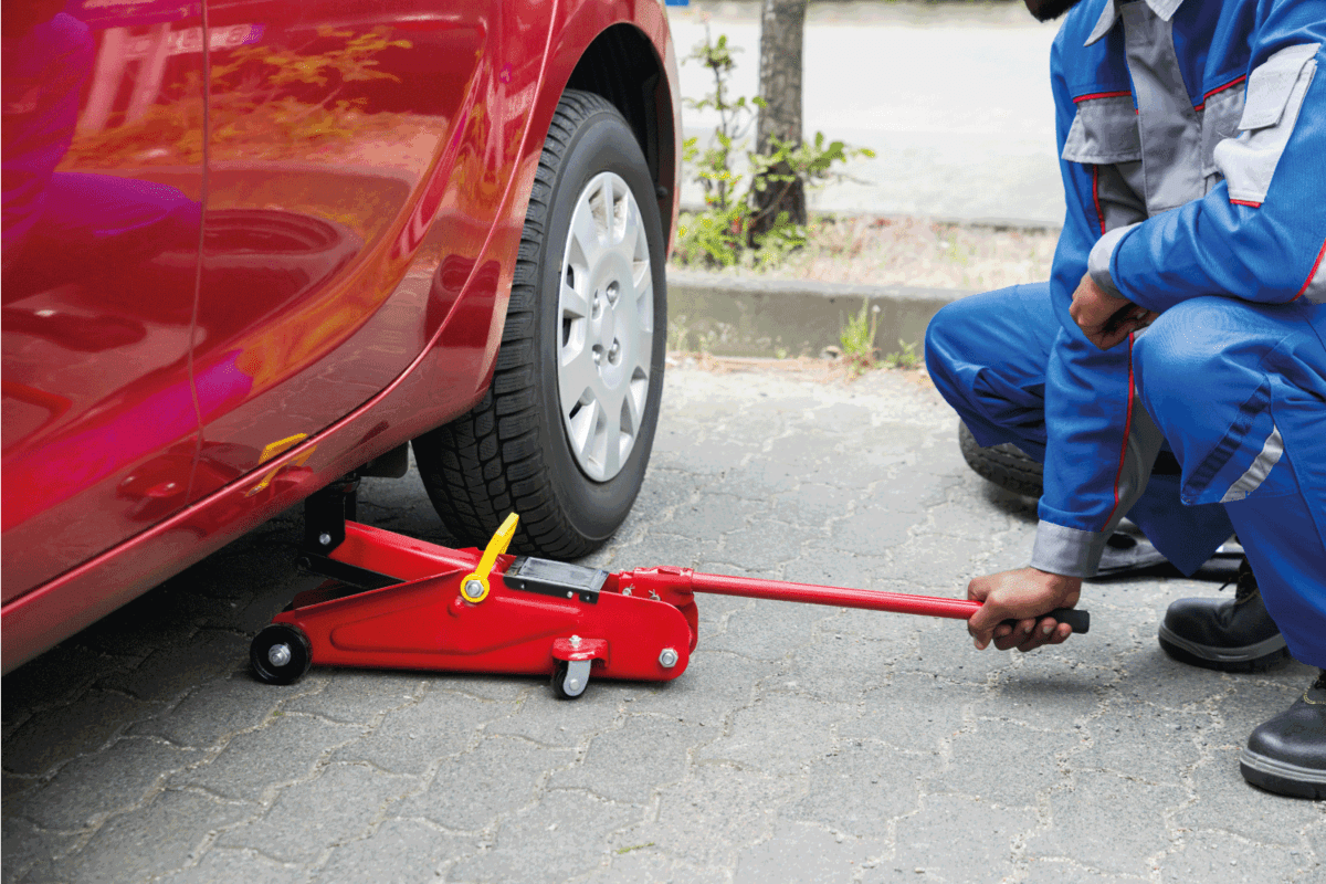 Young Male Mechanic Putting Red Hydraulic Floor Jack under The Car