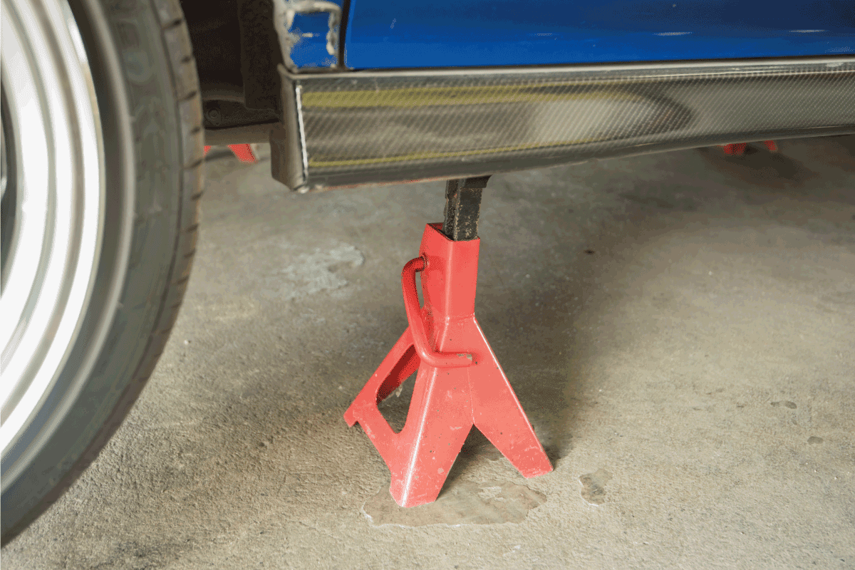 red car jack stand underneath a car for repair. Does Every Car Come With A Jack