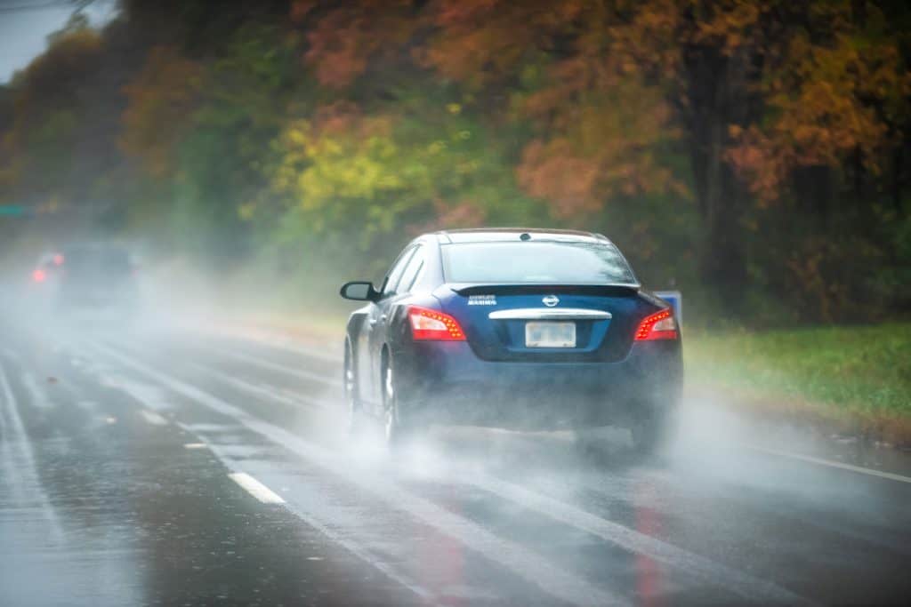 A Nissan Maxima moving down a rainy and slippery highway