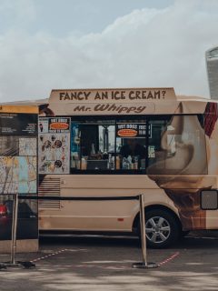 A brown colored ice cream truck parked on the side of a park, When Do Ice Cream Trucks Come? [Here's How To Find Out]