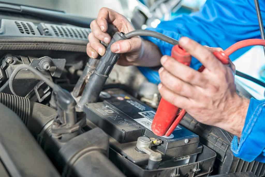A car mechanic uses battery jumper cables to charge a dead battery