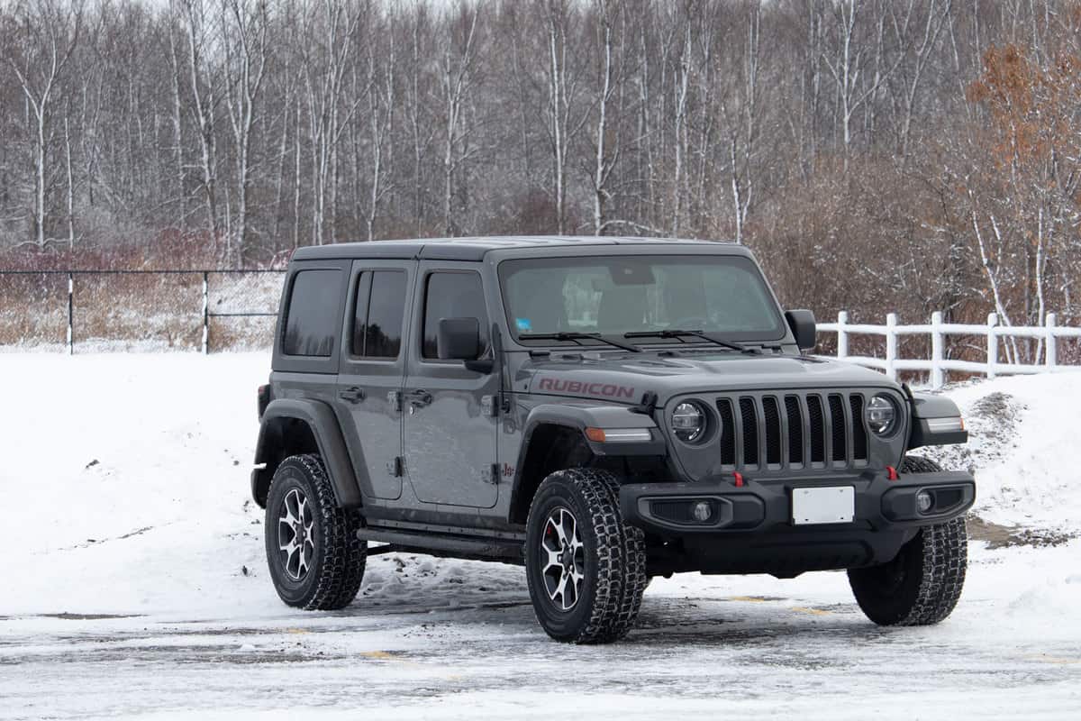 A late model Jeep Wrangler JL Unlimited Rubicon off-road SUV, first seen in the 2018 model year, is parked in a snowy parking lot before trees in winter, How To Insulate A Jeep Hardtop