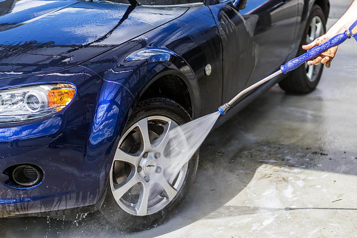 A man washes his blue Mazda MX5 convertible by hand in a car wash