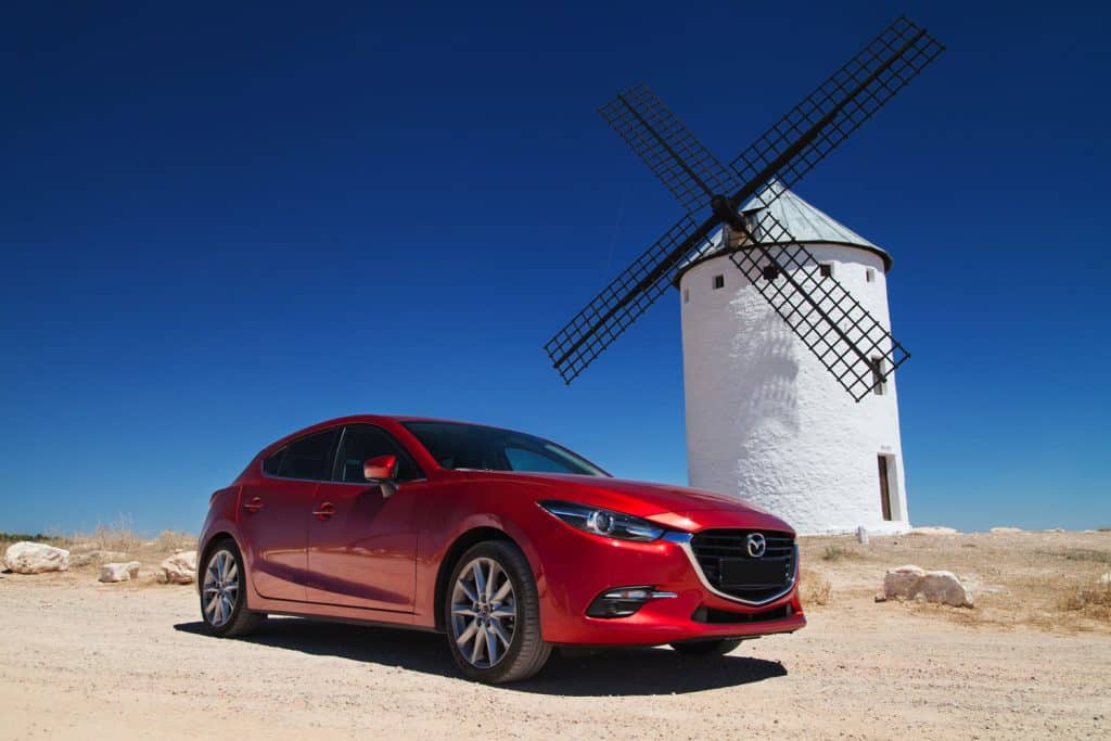 A red Mazda 3 and a windmill on the back photographed at the desert
