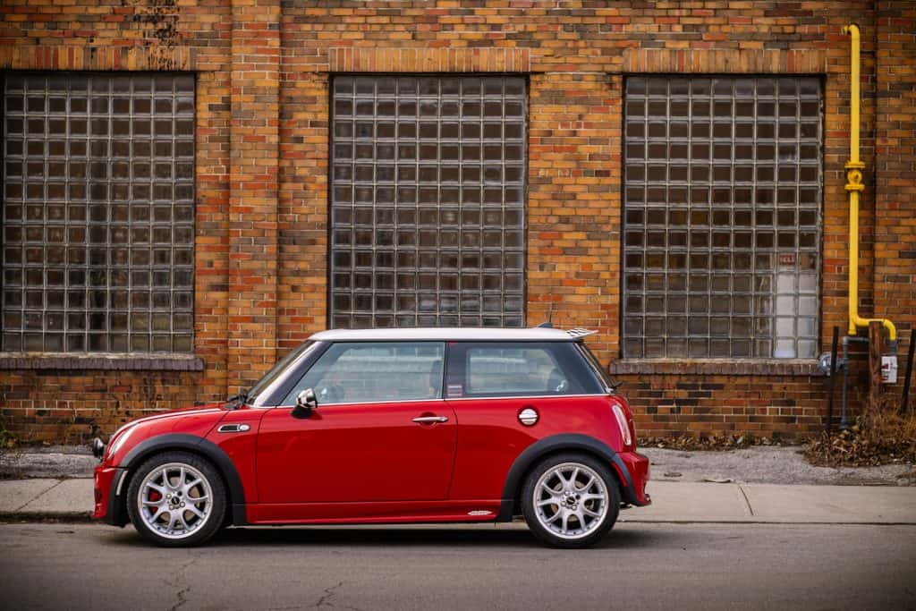 A red colored Mini Cooper parked next to a brick building