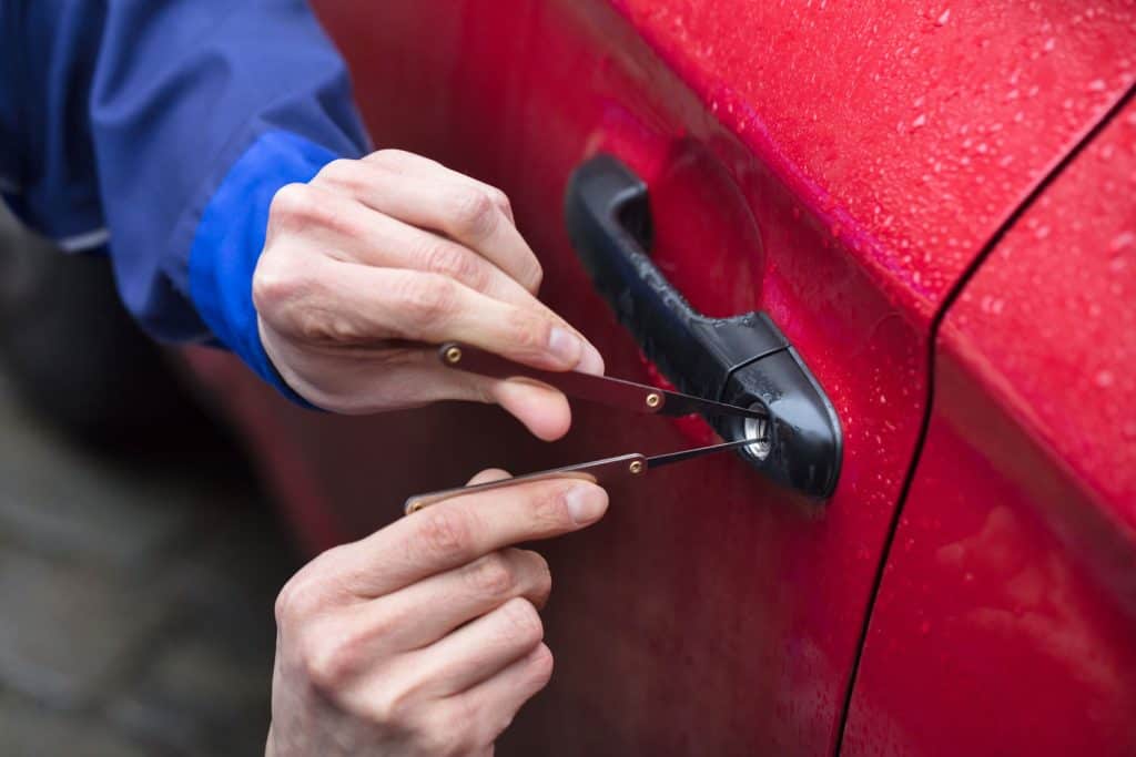Close-up Of Person's Hand Opening Red Car Door With Lockpicker